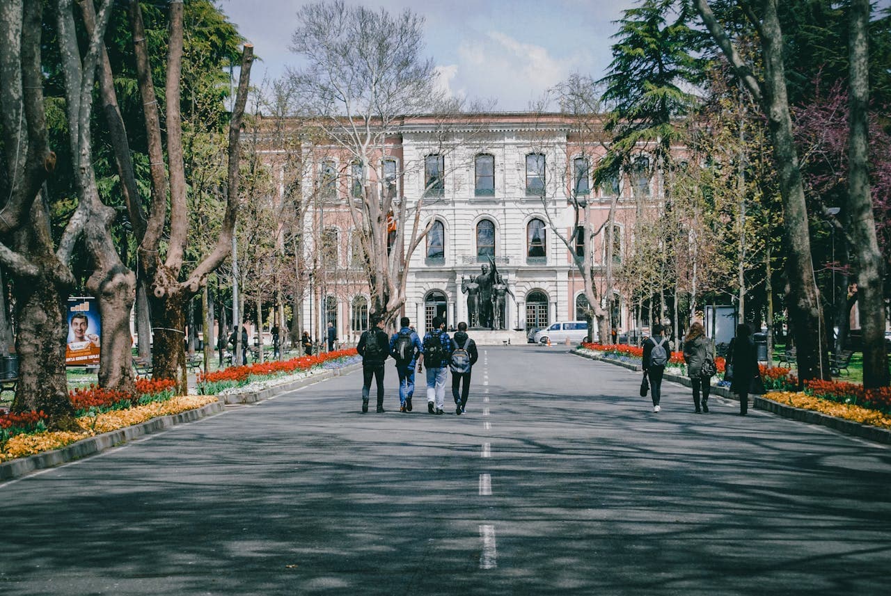 Students walking on a university campus surrounded by trees and spring flowers